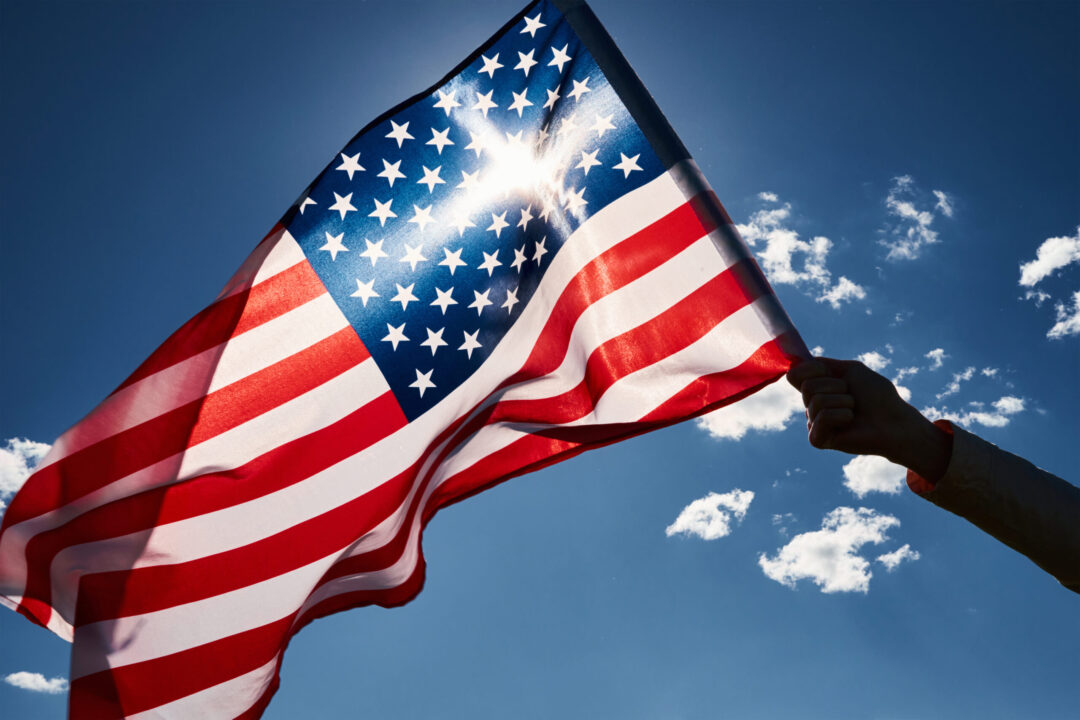A United States flag held against a clear blue sky
