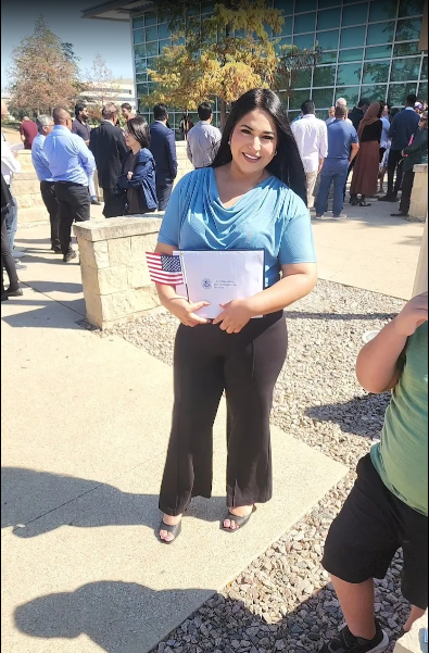 Client standing outside a USCIS office holding an immigration document and a small United States flag