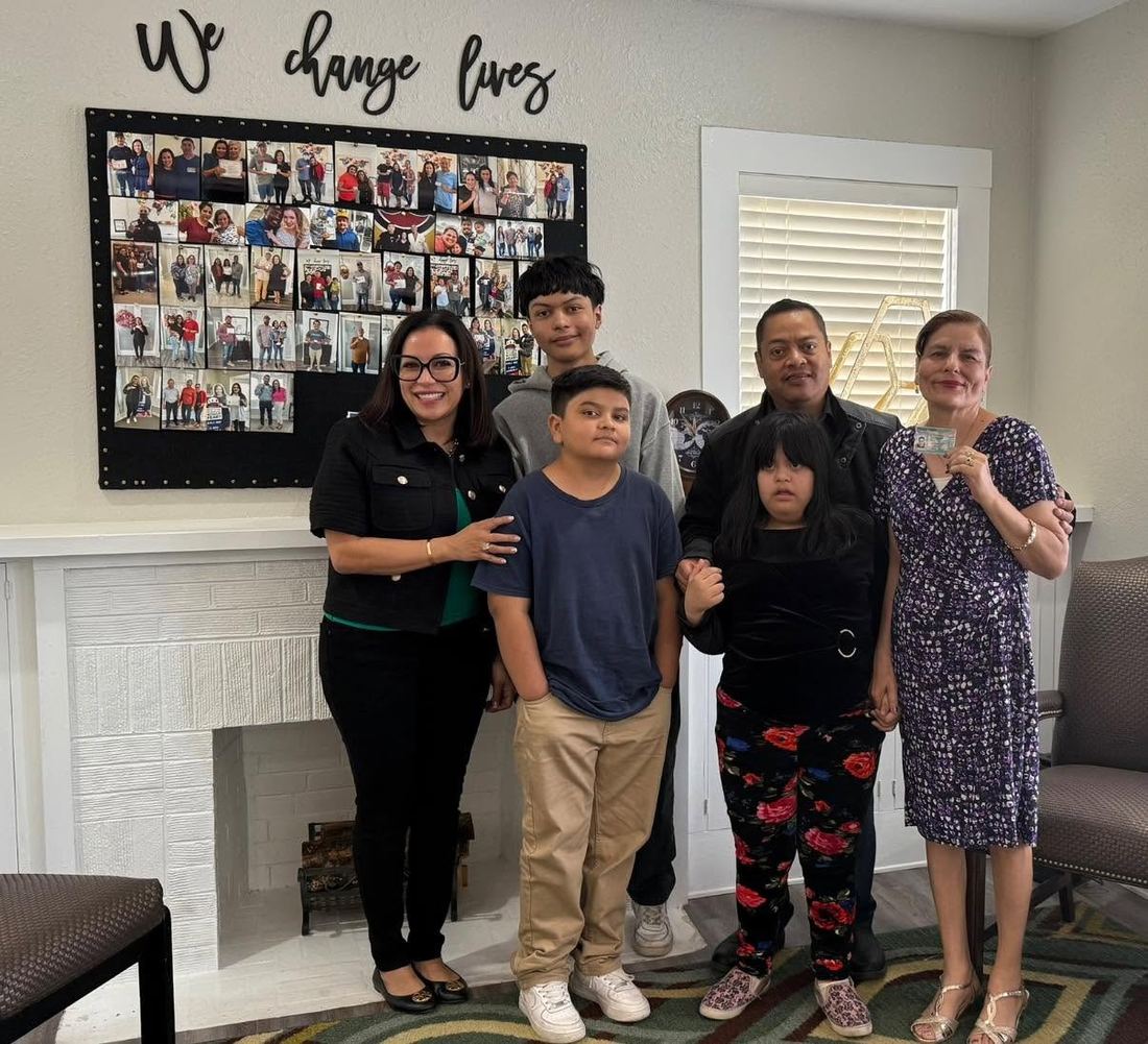 A client family with the team beneath the We Change Lives wall at the Lubbock office