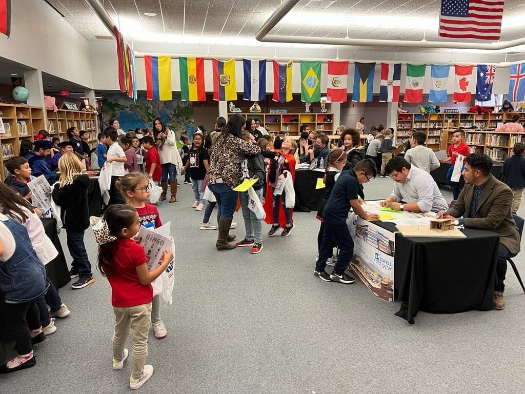 Families at a school resource fair in Lubbock with flags of many nations overhead